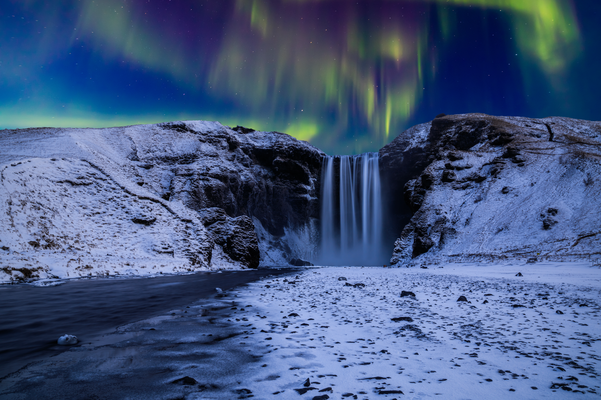 Nordlys over Skógafoss-fossen omgitt av snø i Sør-Island.