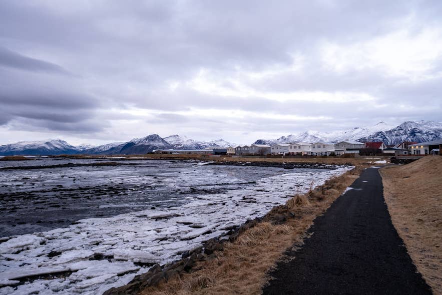 Hofn in winter with snowy mountains, frozen shoreline, and coastal walking path