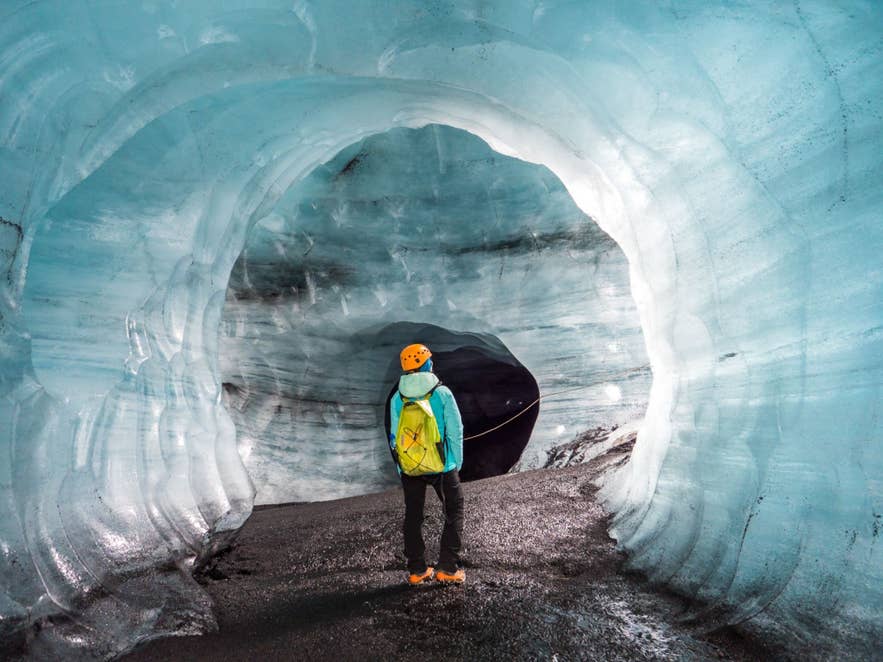 Hiker in a helmet and turquoise jacket at the entrance to the Katla ice cave under Myrdalsjokull Glacier.