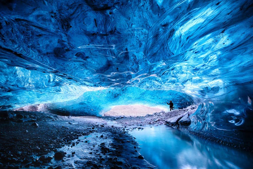 Visitor deep inside a blue ice cave beside a meltwater stream, where safety depends on the operator's own checks.