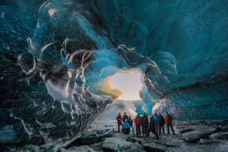Tour group posing at the sunlit mouth of a crystal ice cave in Iceland.