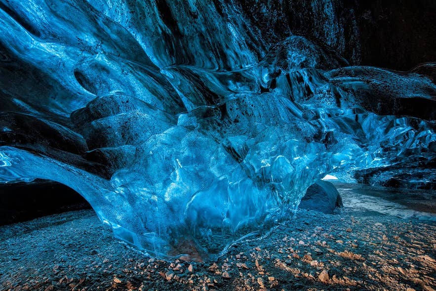 Deep blue glacier ice arching over a gravel floor inside an Iceland ice cave.