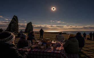 Travelers viewing a solar eclipse from the dramatic coastline of the Snaefellsnes Peninsula.