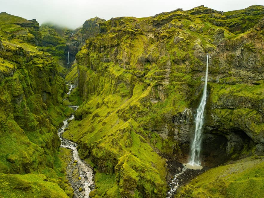 Moss-covered canyon in Iceland with steep green cliffs, narrow river streams, and waterfalls dropping from rocky hillsides.