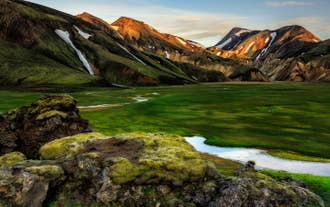 A lush green valley surrounded by colorful rhyolite mountains in the Icelandic Highlands.