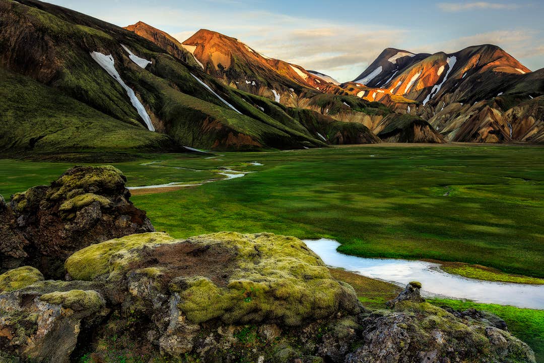A lush green valley surrounded by colorful rhyolite mountains in the Icelandic Highlands.