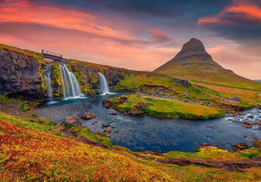Kirkjufellsfoss Waterfall in Iceland, flowing over mossy cliffs with Kirkjufell Mountain in the background, captured during a colorful autumn sunset.