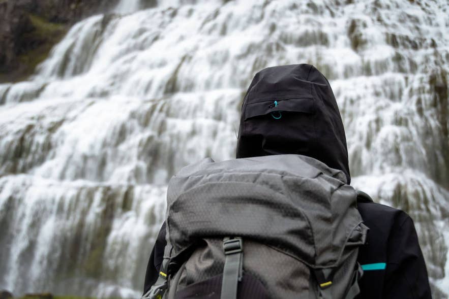 Traveler with a backpack standing in front of a powerful waterfall in Iceland surrounded by mist and rugged nature.