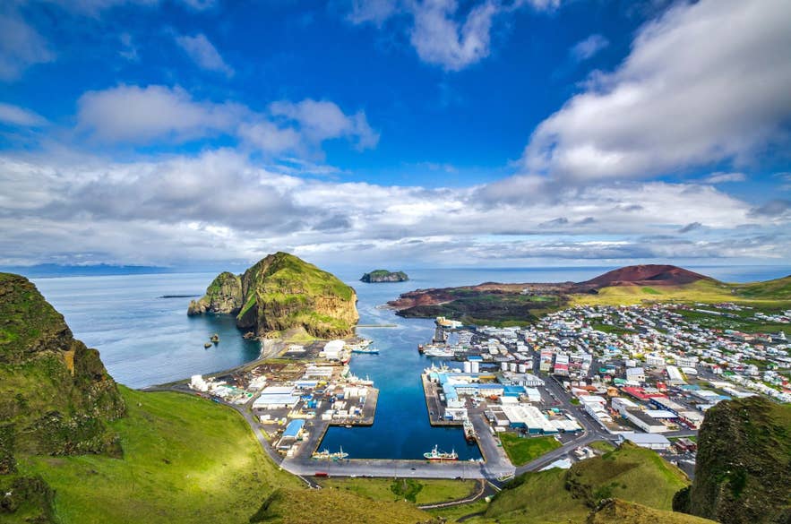 Aerial view of Heimaey island in Vestmannaeyjar, Iceland with dramatic cliffs, colorful volcanic landscapes, and a coastal harbor.
