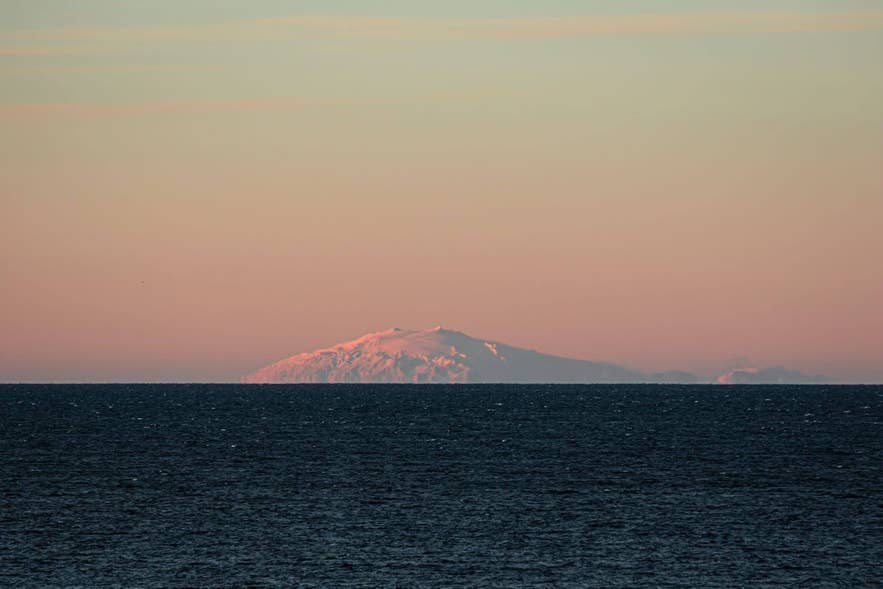 Snaefellsjokull glacier volcano rises above the ocean at sunset on the Snaefellsnes Peninsula in Iceland.