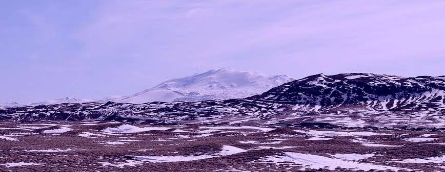 Snow-dusted slopes of Mount Hekla stretch across a rugged volcanic landscape beneath a soft purple sky.