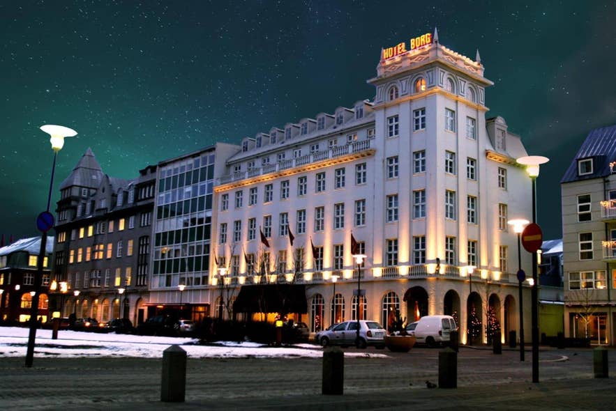 Hotel Borg glows with warm lights under a starry night sky, with snow patches and parked cars along the quiet street.