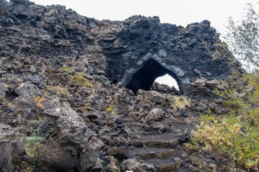 A lava rock archway at Dimmuborgir with a rocky path and some plants around it.