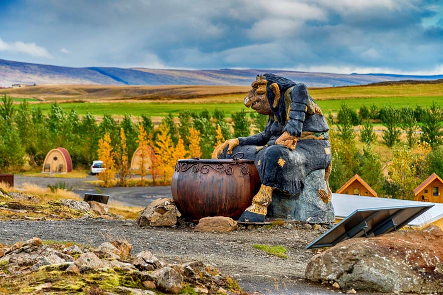Icelandic troll statue of Grýla beside a cauldron in rural Icelandic landscape under dramatic clouds Icelandic troll statue of Grýla beside a cauldron in rural Icelandic landscape under dramatic clouds