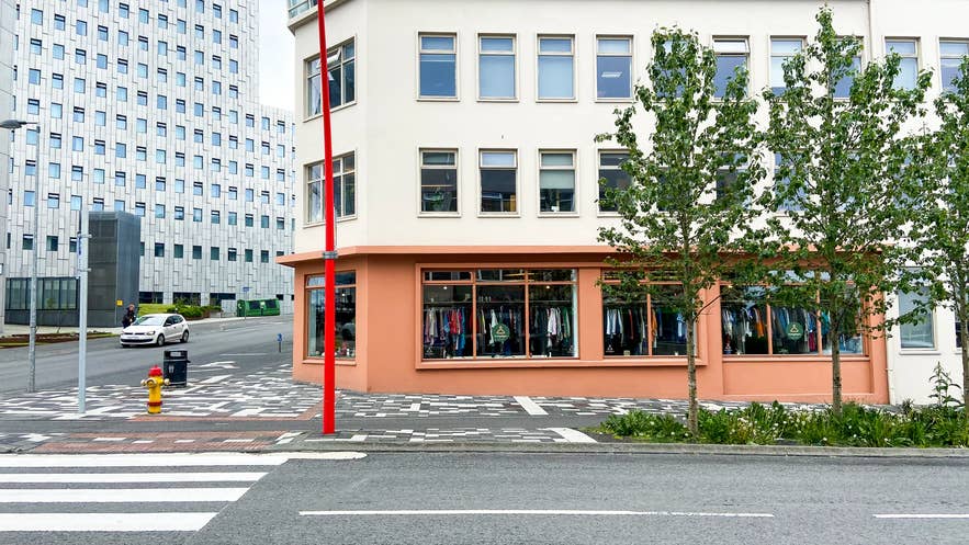 Street view of a second-hand clothing store in downtown Reykjavik with large display windows, peach-colored exterior walls, and modern buildings nearby.