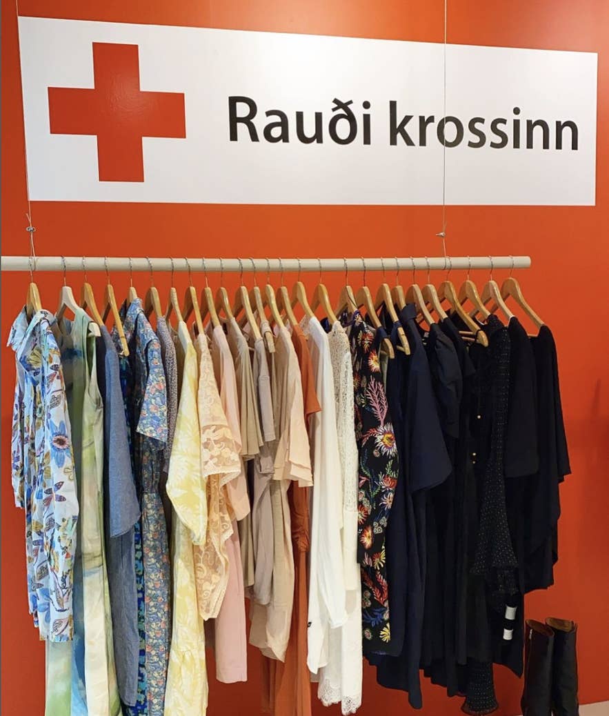 Clothing rack inside a Red Cross Store in Iceland beneath a Raudi krossinn sign with colorful secondhand garments on display.
