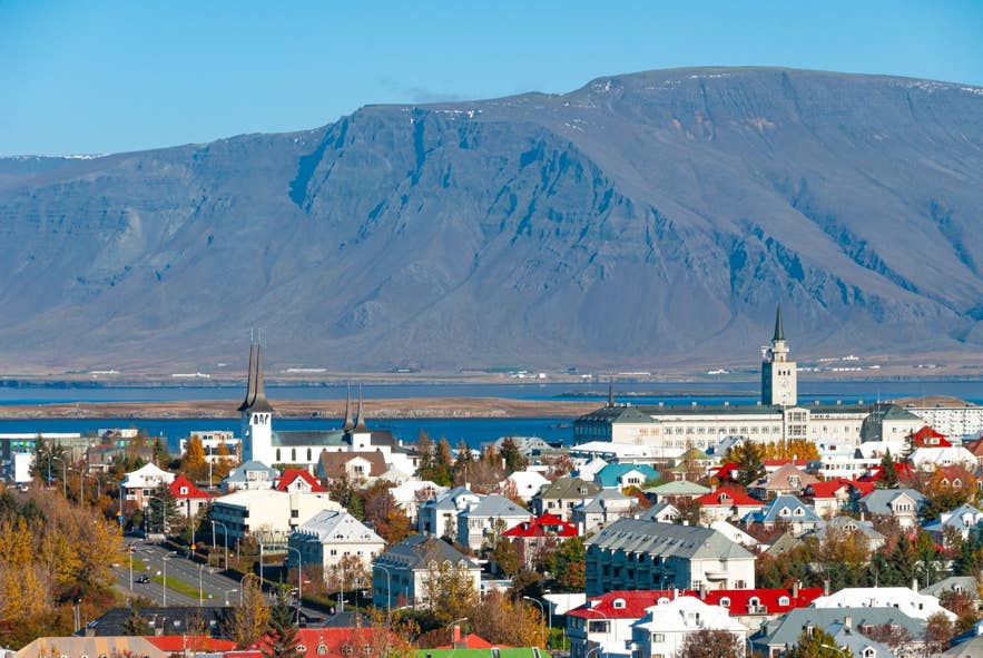 View of Reykjavik with Hallgrimskirkja church, colorful rooftops, Faxafloi Bay, and Mount Esja rising in the background on a clear day.
