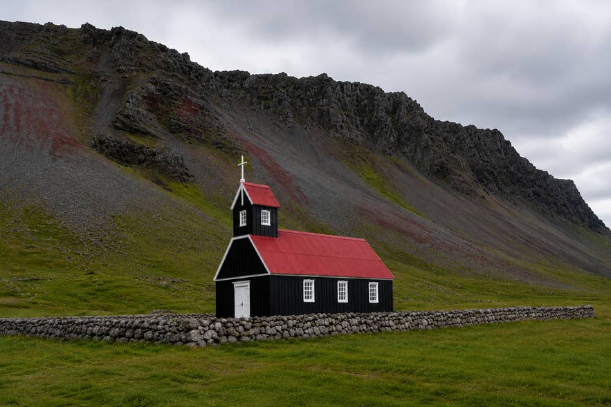 Saurbaejarkirkja Church with its red roof and black body in the Westfjords of Iceland