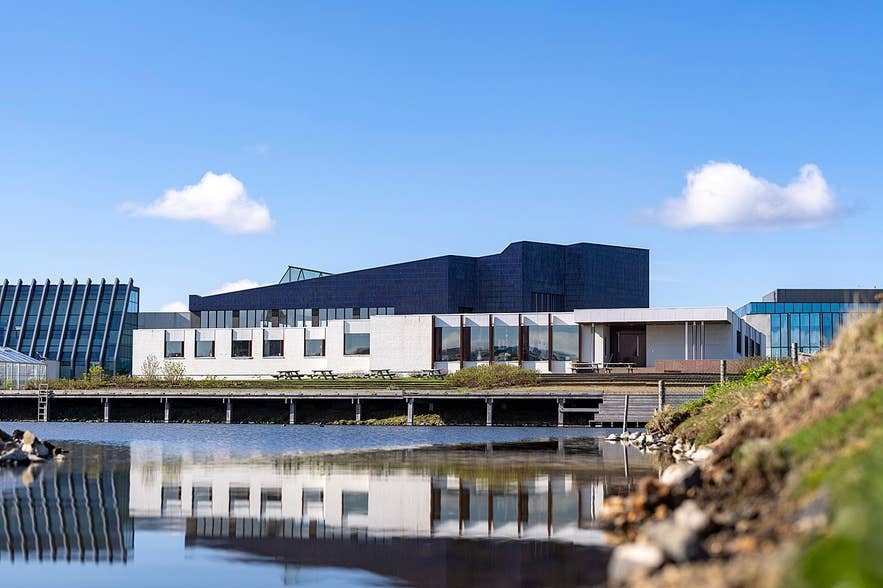 Nordic House in Reykjavík with modern white and blue geometric design, glass windows, and pond reflection under clear sky.