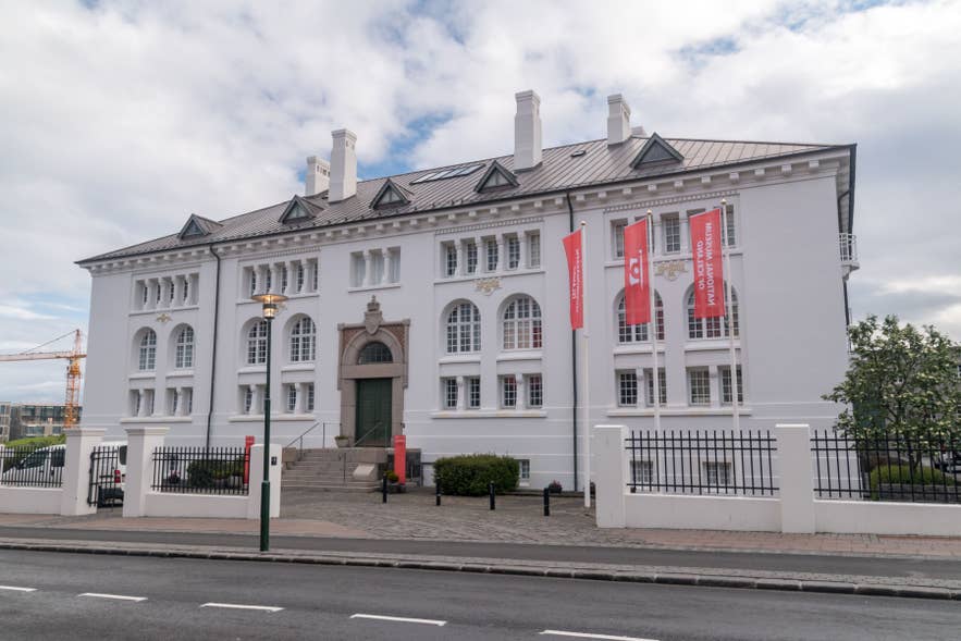 National Museum of Iceland with white neoclassical facade, arched windows, green door, and red banners along the street.