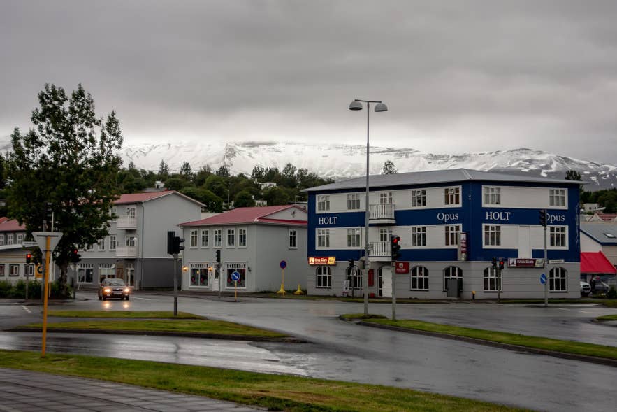 Regennasse Straße in Akureyri mit schneebedeckten Bergen im Hintergrund.