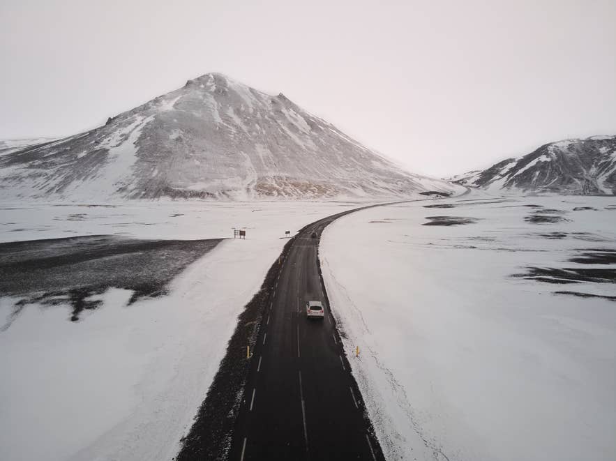 Car driving on a snowy road through with Eastfjords mountains in the background