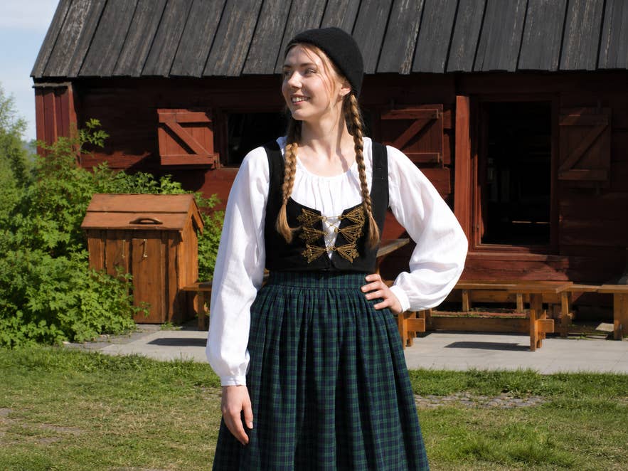 Woman wearing the Icelandic upphlutur national costume in front of a traditional wooden house in Iceland