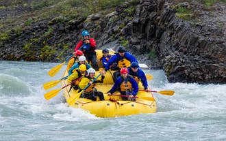 A group of rafters paddles a yellow raft through rapids on the Hvita river during a whitewater rafting tour in Iceland.