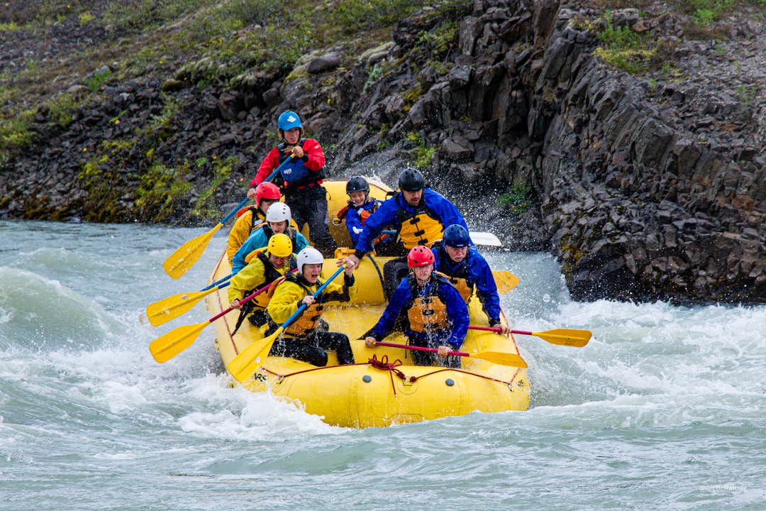 A group of rafters paddles a yellow raft through rapids on the Hvita river during a whitewater rafting tour in Iceland.