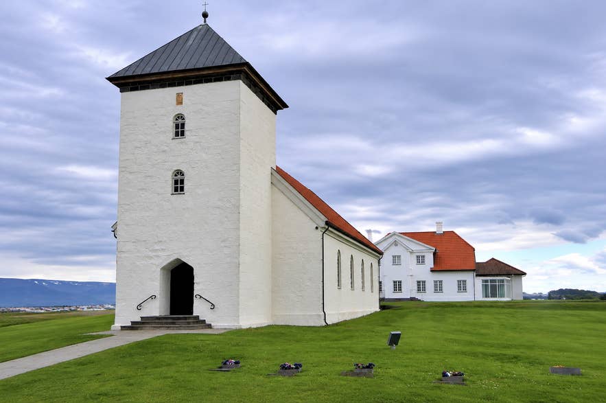 Bessastadakirkja Church in Iceland with green lawn under a cloudy sky.