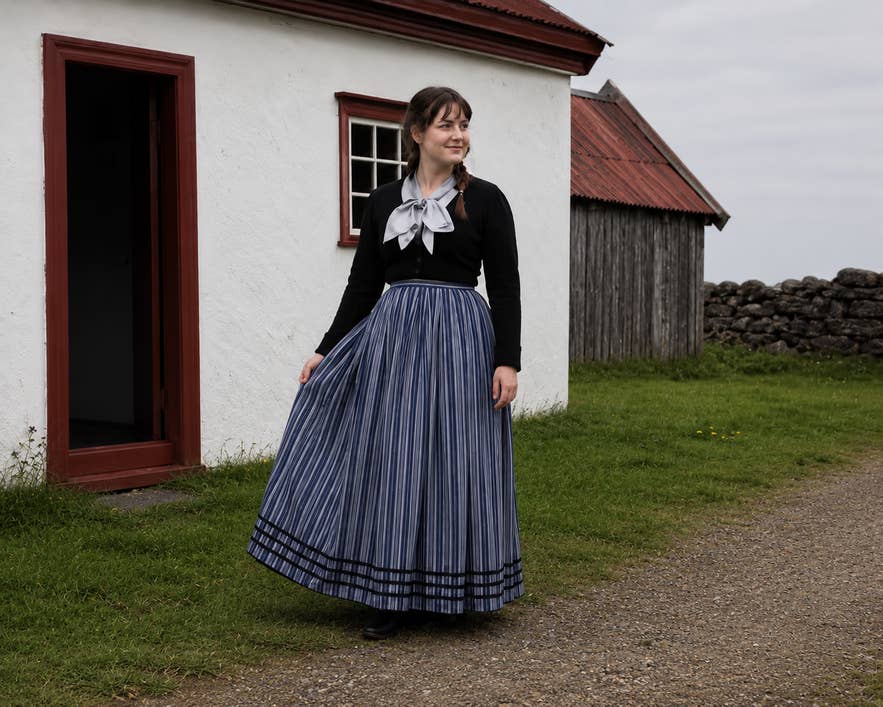 Woman wearing the Icelandic peysuföt national costume beside a white house in Iceland