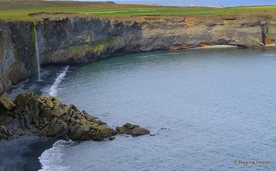 Steep coastal cliffs at Ketubjorg with a narrow waterfall dropping into a rocky cove beside the sea.
