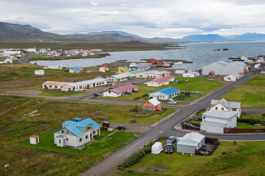 View over the coastal village of Skagastrond, with colorful houses, a small harbor, surrounding mountains, and the sea in the distance.