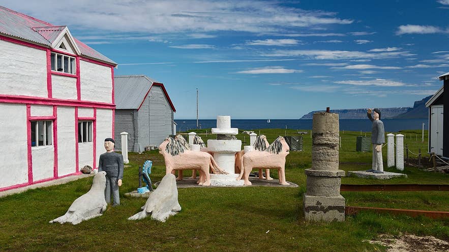 Colorful sculptures and buildings at Samuel Jónsson Art Farm, Selárdalur Valley, Iceland, with ocean and cliffs beyond