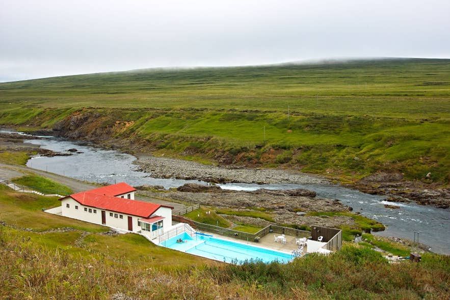 Selárdalur outdoor swimming pool in Iceland, fed by natural hot springs, beside river and grassy valley hills.