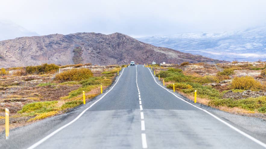 Road through Iceland’s Golden Circle with volcanic hills and a car driving in the distance.