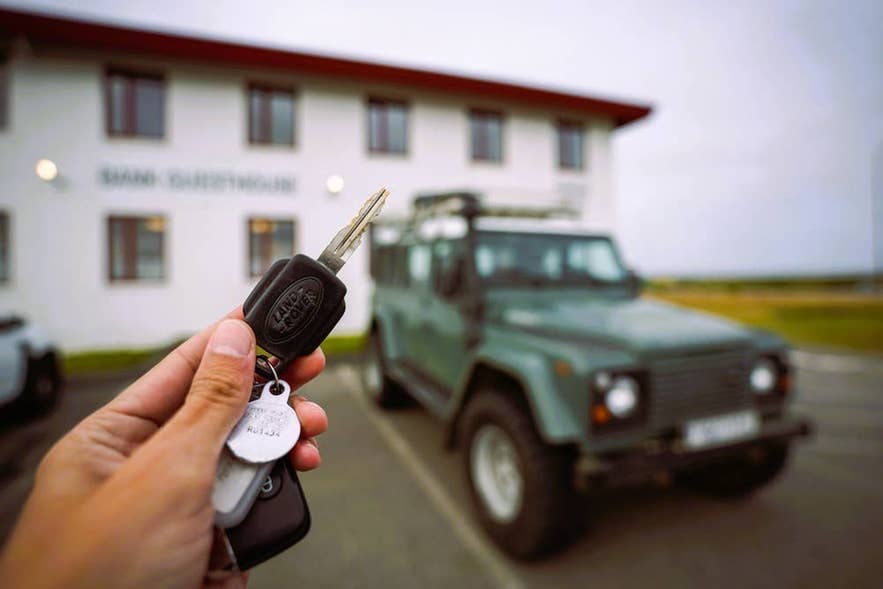 A person holding car keys in front of a four-wheel-drive rental vehicle in Iceland.