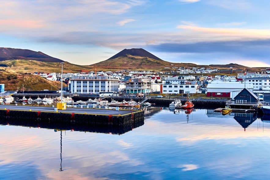 View of Vestmannaeyjar harbor with fishing boats, colorful buildings, and Eldfell volcano rising above the town in Iceland.