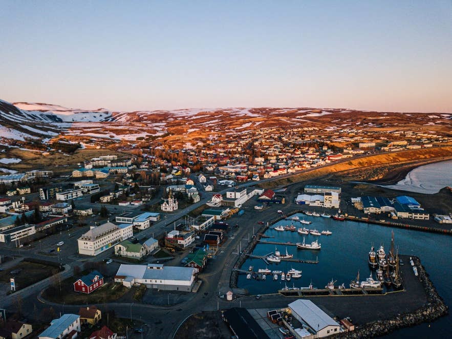 Diese Luftaufnahme zeigt den Hafen von Husavík in Nordisland mit seinen bunten Gebäuden und verschneiten Hügeln im Licht des Sonnenuntergangs.