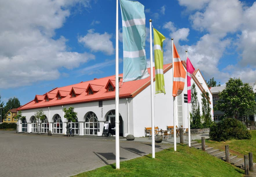 Hafnarborg cultural center in Hafnarfjordur, with colorful flags, a white facade, and a red roof beneath a bright summer sky.
