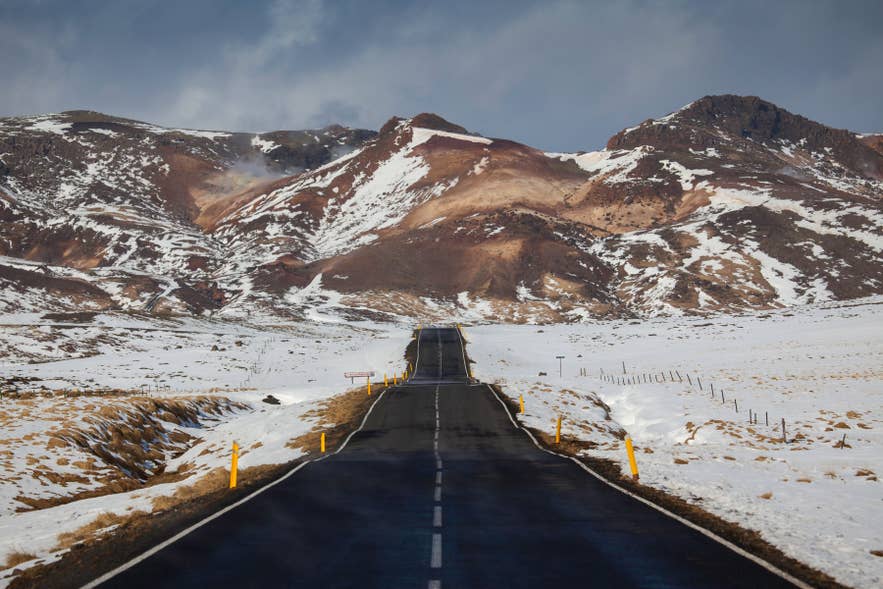 Straight road to Krýsuvík geothermal area, Reykjanes Peninsula, with snow‑covered mountains in winter.