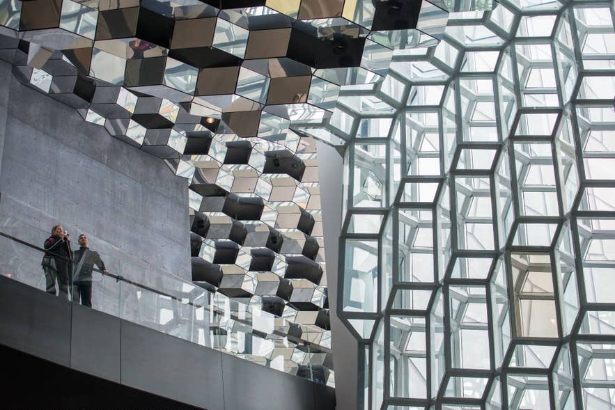 Visitors stand inside Harpa Concert Hall in Reykjavik, surrounded by mirrored ceiling panels and the building’s iconic geometric glass facade.