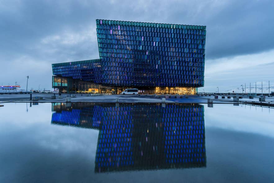 Harpa Concert Hall in Reykjavik reflects in a still pool, showcasing its colorful glass facade along the waterfront.
