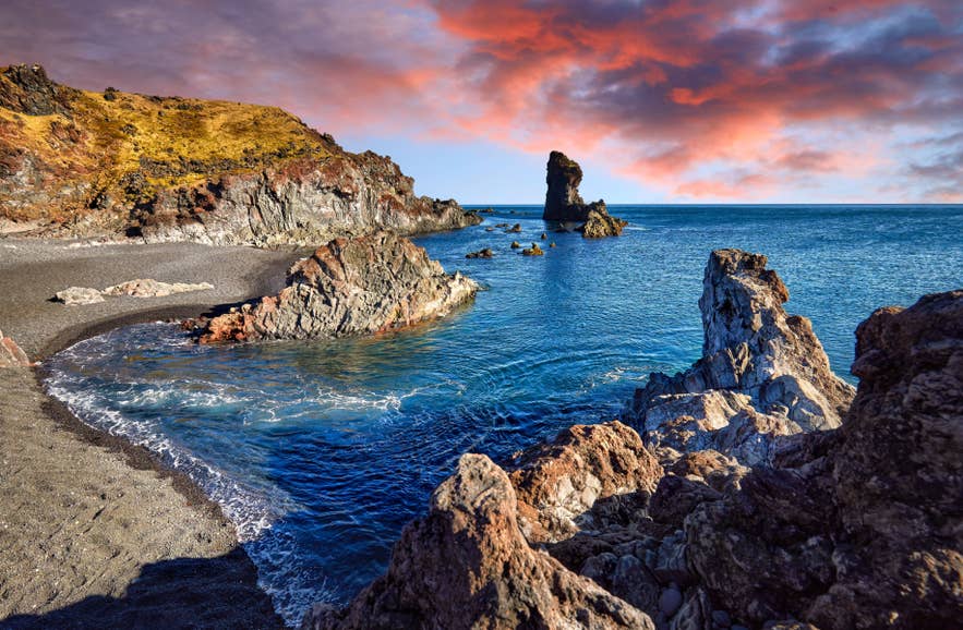 The Londrangar sea stacks rise from the Atlantic Ocean along the rugged Snaefellsnes Peninsula coastline under a colorful Icelandic sky.