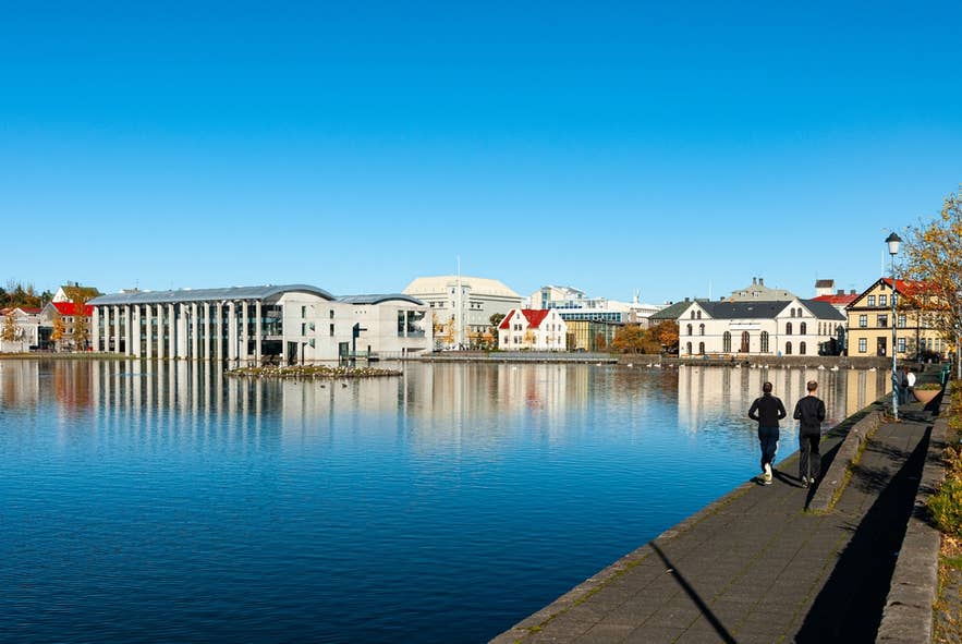 Walkways around Tjornin Pond in Reykjavik with runners and joggers under a clear blue sky.