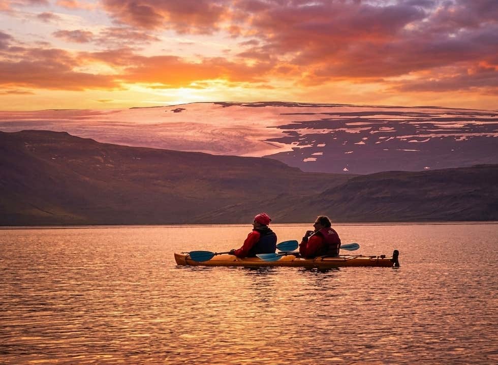 Two paddlers glide across a calm fjord in a tandem sea kayak beneath the midnight sun near Arskogssandur in North Iceland.