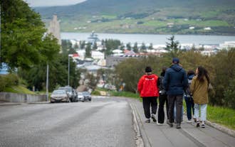 Visitors walk down a street in Akureyri toward the fjord and a docked cruise ship.