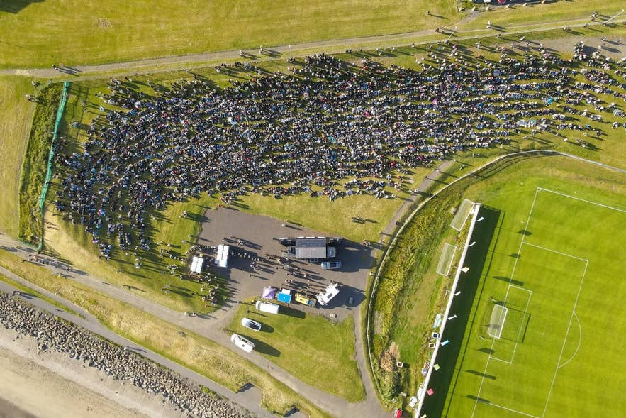 Aerial view of crowds gathered by the coast for Irish Days in Akranes, with a sports field and event area nearby. Aerial view of crowds gathered by the coast for Irish Days in Akranes, with a sports field and event area nearby.