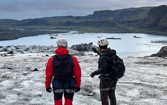 Two hikers in helmets pause to look out over the ice on a Solheimajokull Glacier hike on the South Coast.