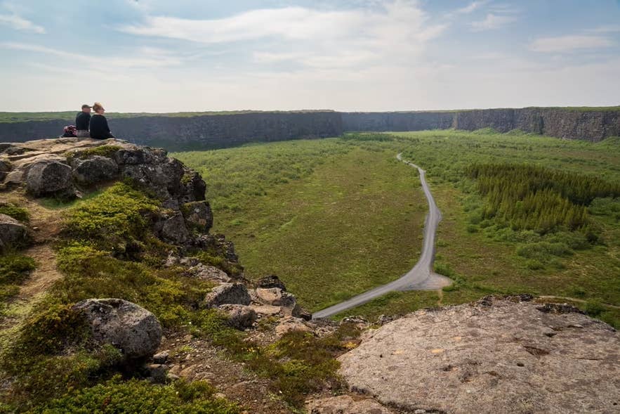 Asbyrgi Canyon with visitors on a cliff overlooking the horseshoe-shaped valley and winding road in North Iceland.